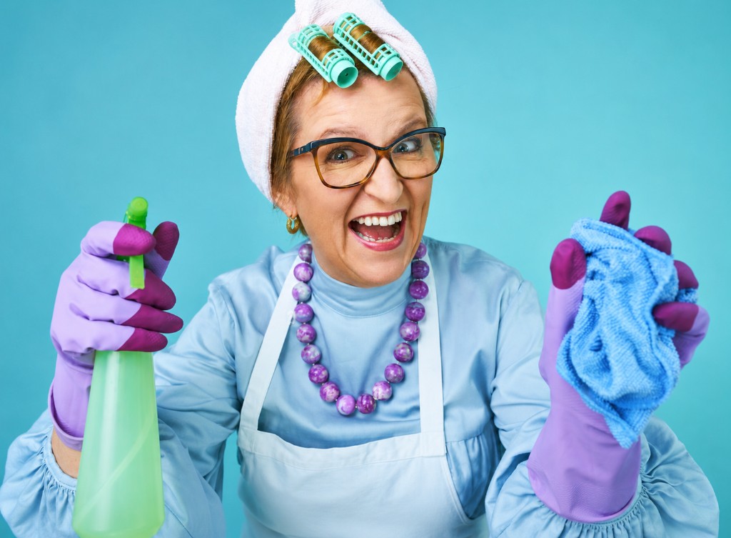 Professional cleaner in apron and purple gloves with spray bottle and cloth — approachable commercial cleaning brand photography.